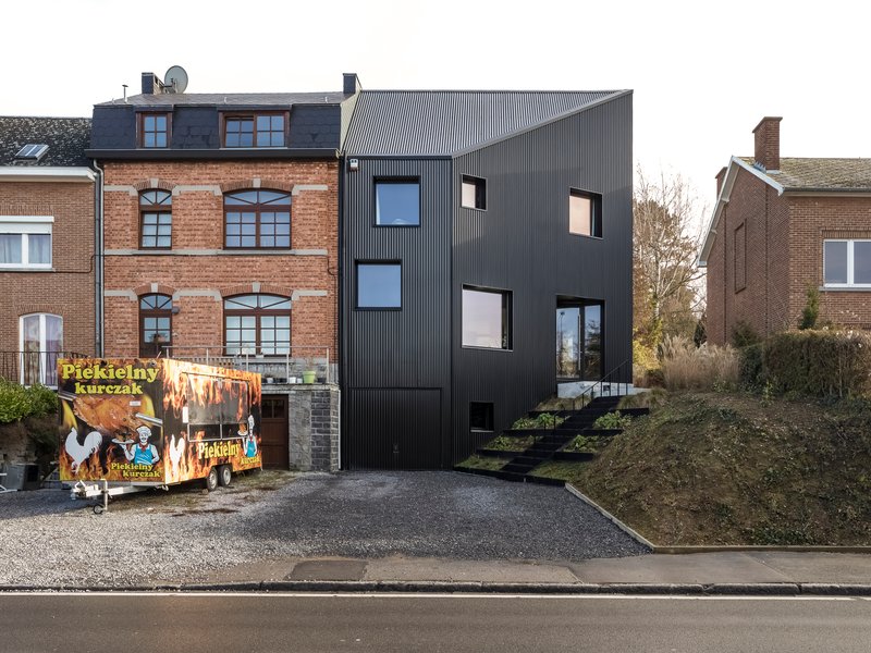 Street view of the black corrugated metal facade nestled between brick buildings with a food truck parked in front