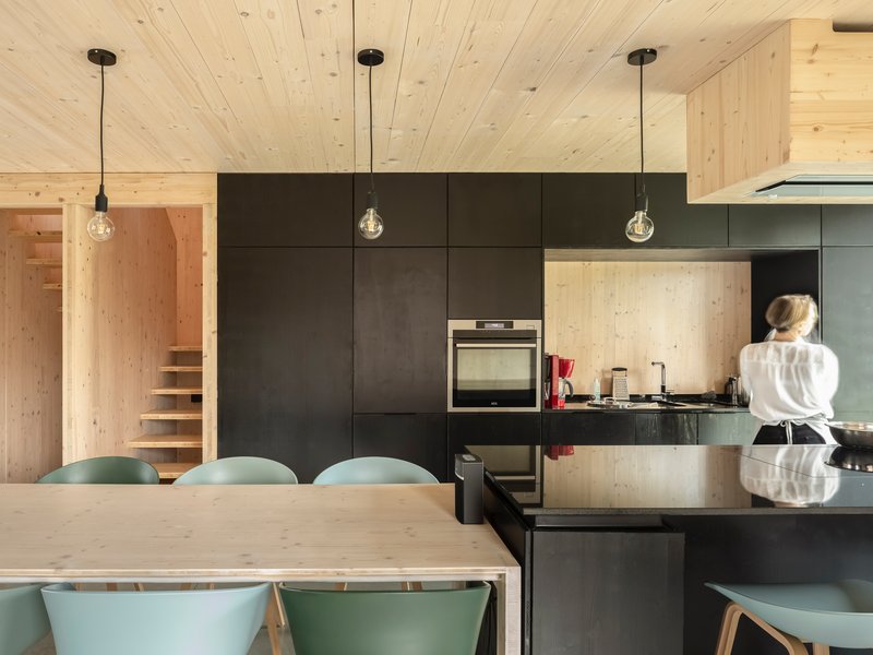 Kitchen with dark steel cabinets and timber panels flanked by a visible timber staircase beyond