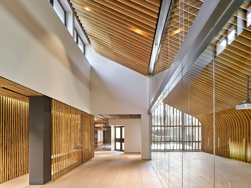 Double-height lobby with timber slatted ceiling and glass-walled mezzanine level above pale wood flooring