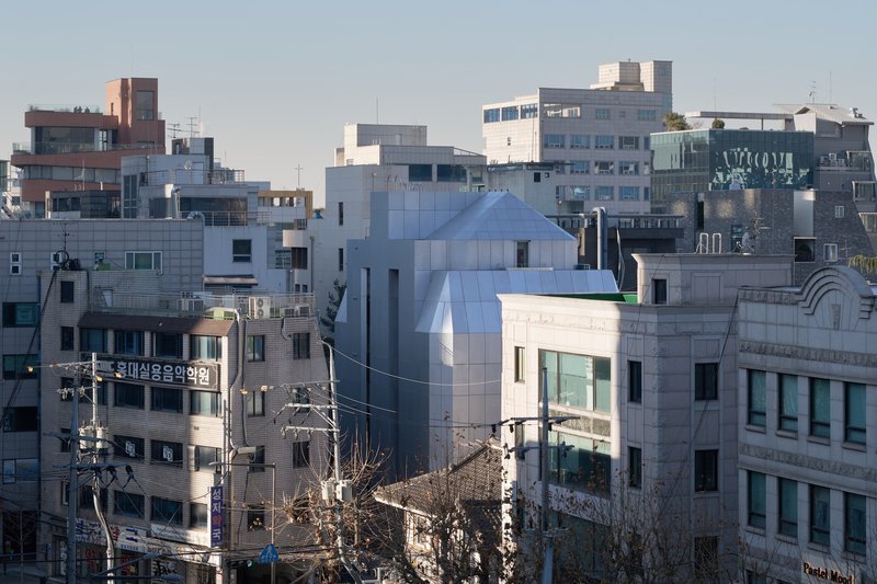 Elevated view of the angular white volume with pyramidal roof amid the dense urban block