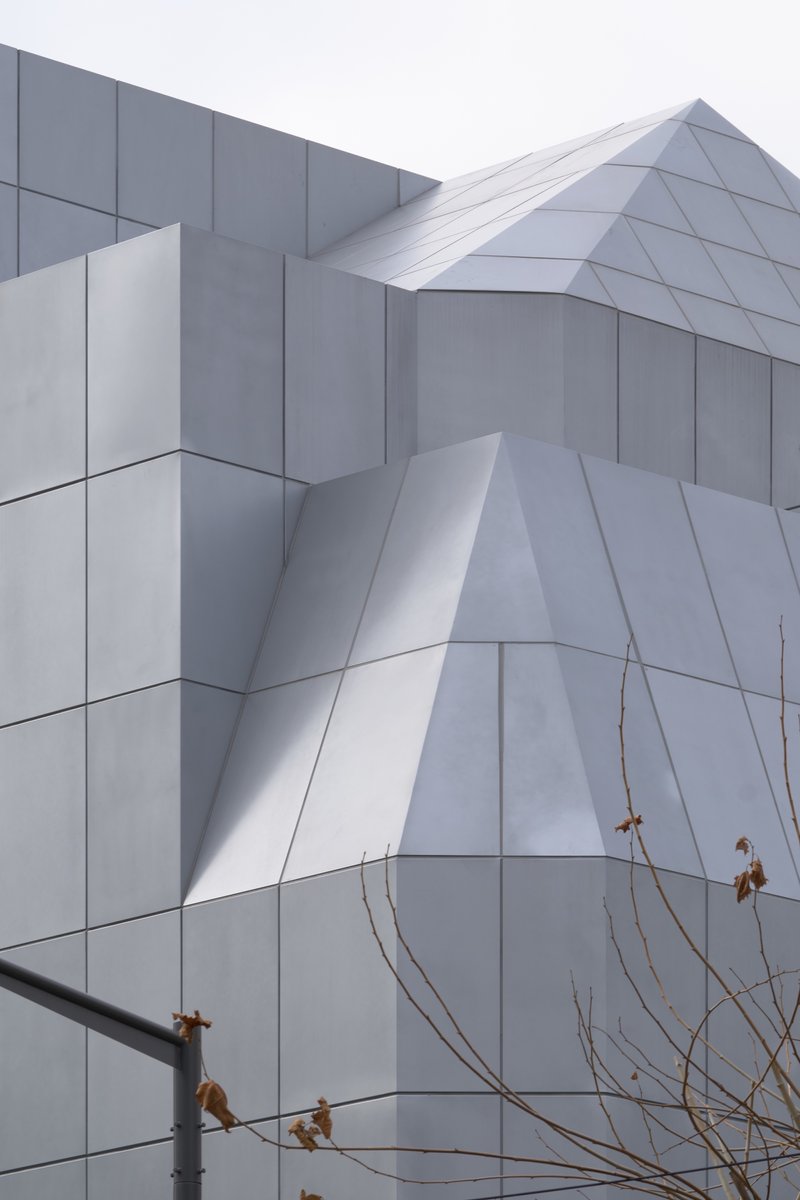 Close-up of the folded white panel facade with bare winter branches in the foreground