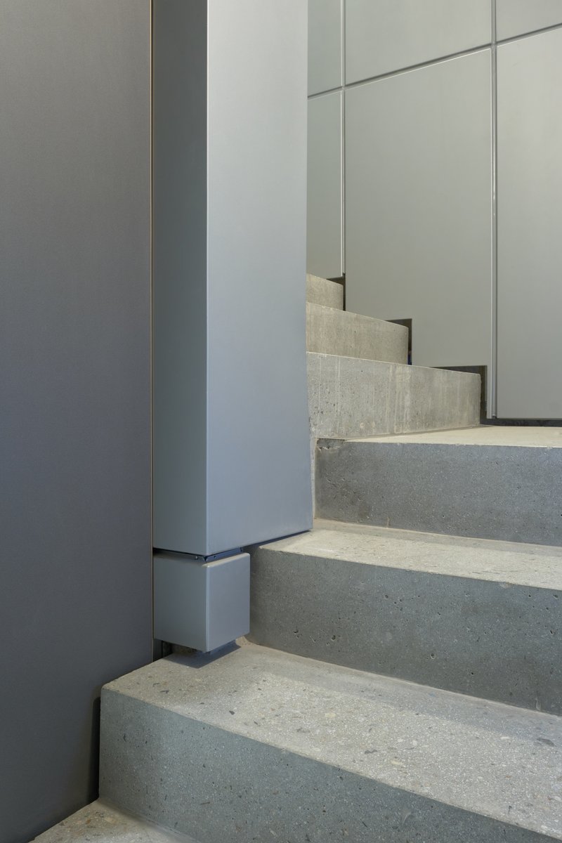 Concrete stair treads meeting grey metal wall panels and vertical column in natural light