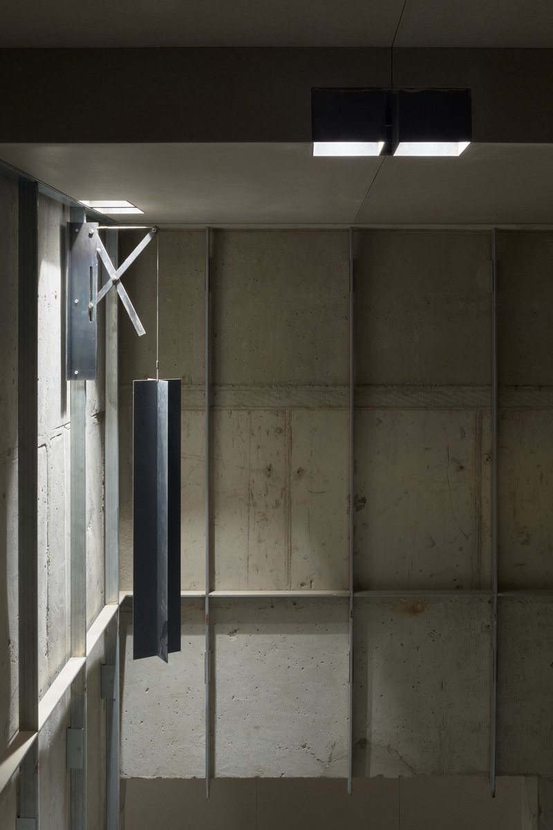 Interior view of exposed concrete wall panels with vertical steel columns and suspended lighting fixtures