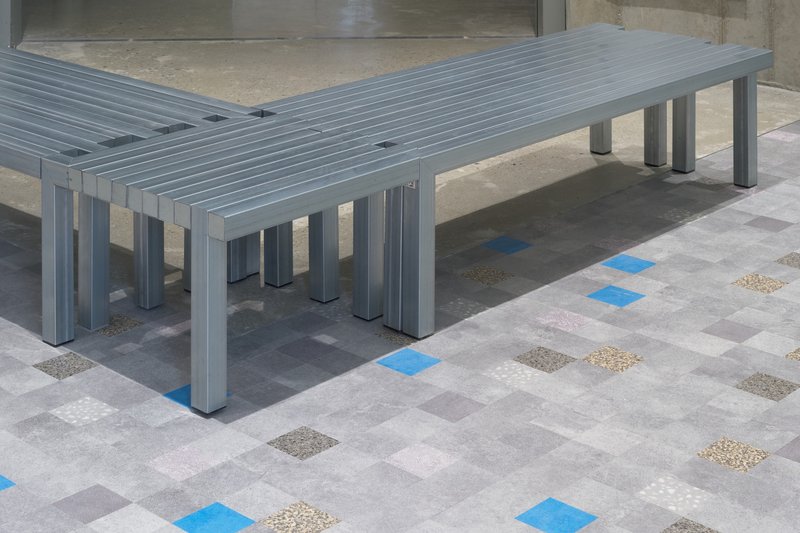 Grey slatted benches on multicolored terrazzo tile floor with blue and beige inlays