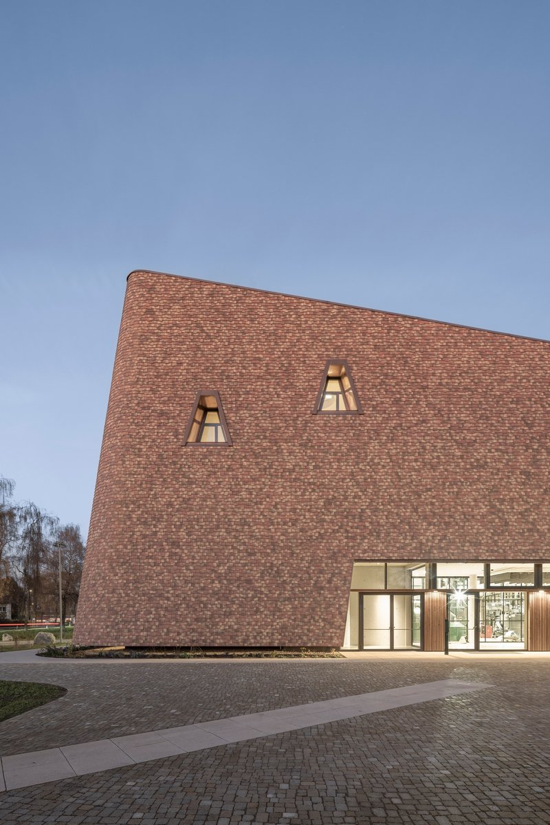 Brick facade with illuminated trapezoidal windows above the glazed entrance at twilight
