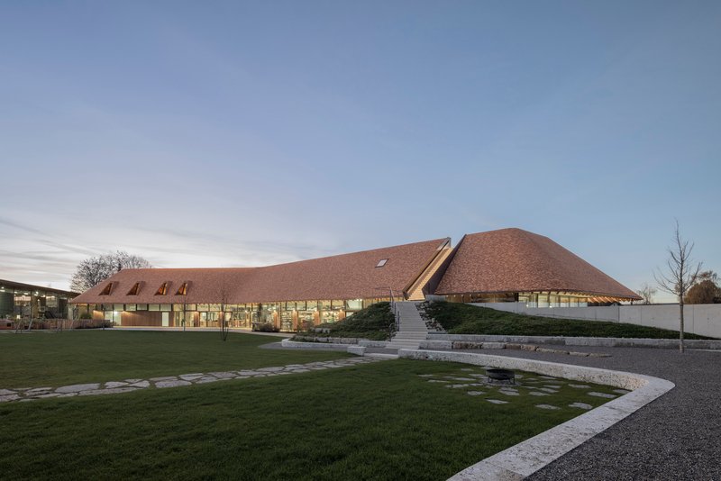 Low-angled view of the undulating shingled roof volumes across a lawn at dusk