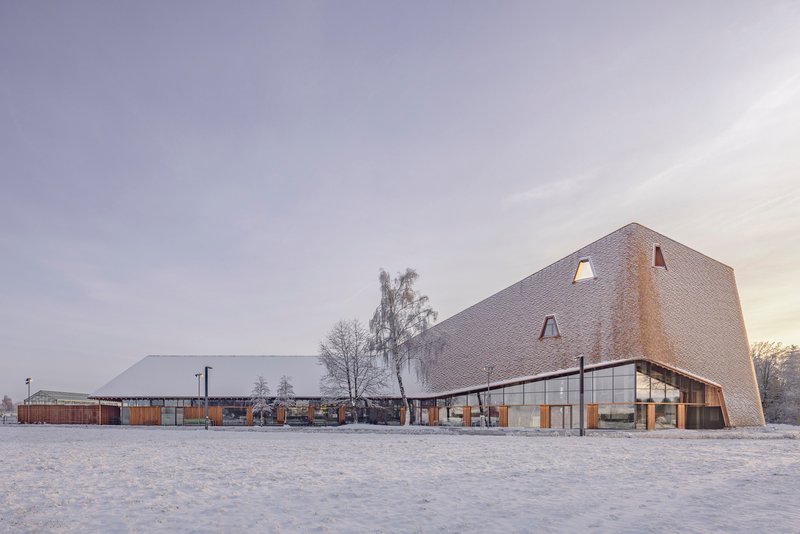 The shingled volume and linear pavilion across a frozen courtyard at dawn