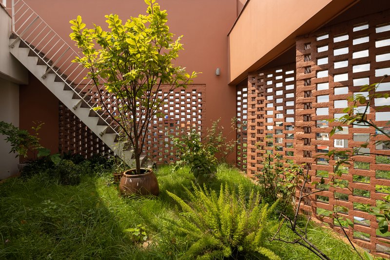 Planted courtyard garden with perforated brick walls and a steel staircase in afternoon sun