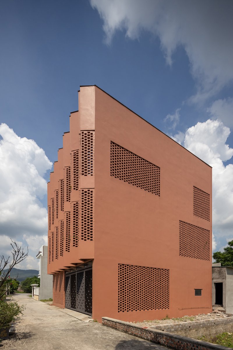 Street view of the perforated brick facade with stepped upper floors against white clouds