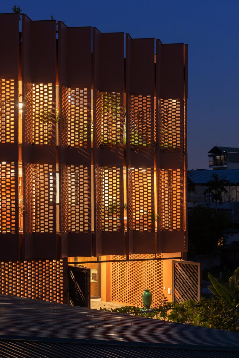 Perforated brick facade with backlit panels and vertical louvers illuminated at dusk