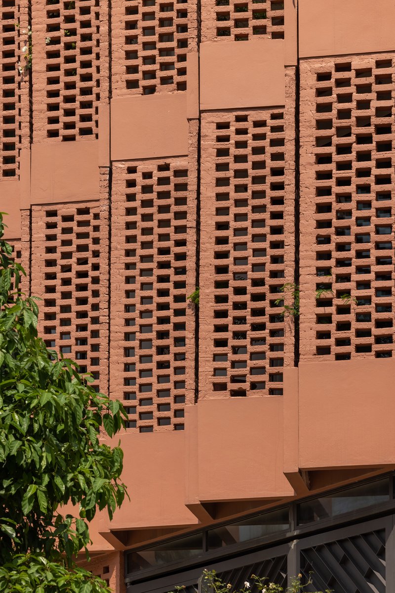 Close-up of the terracotta screen wall with rectangular perforations and exposed cladding joints beside green leaves