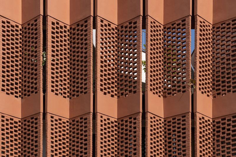 Repeating terracotta lattice panels in warm sunlight with glimpses of greenery through the openings