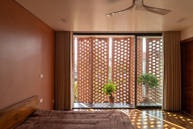Bedroom with perforated brick screen walls filtering sunlight onto potted plants and patterned floor