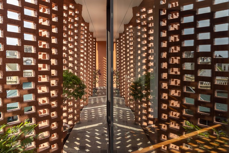 Corner courtyard enclosed by curved perforated brick walls casting dappled shadows on the paving