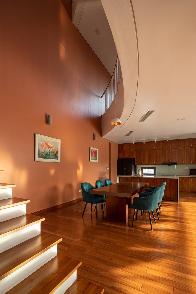 Open dining area with illuminated stair treads and curved terracotta walls under warm evening light