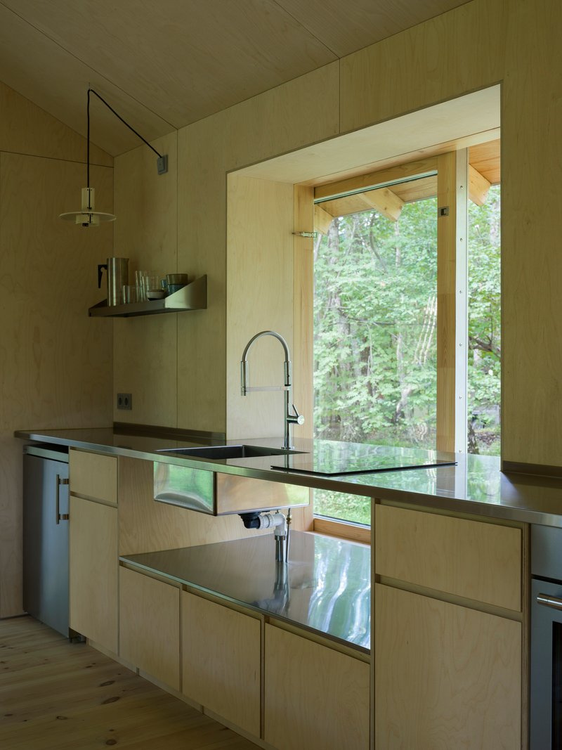 Kitchen with plywood cabinetry, dark countertop, and large window framing summer foliage