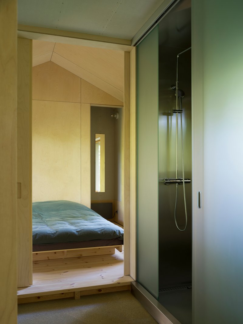 Bathroom with glass shower enclosure and view through doorway to bedroom with blue bedding