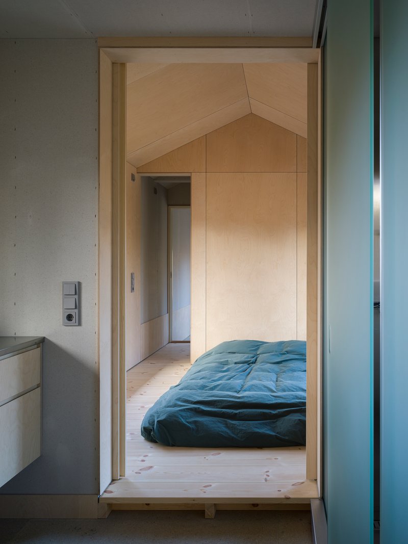 Doorway leading to a raised bedroom platform with plywood lining and a green futon