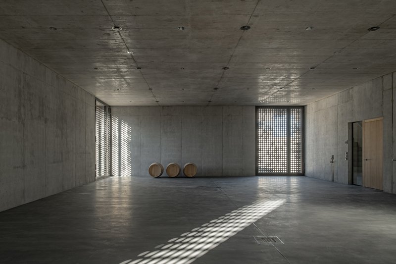 Bare concrete interior with wooden barrels and light filtering through perforated screen openings