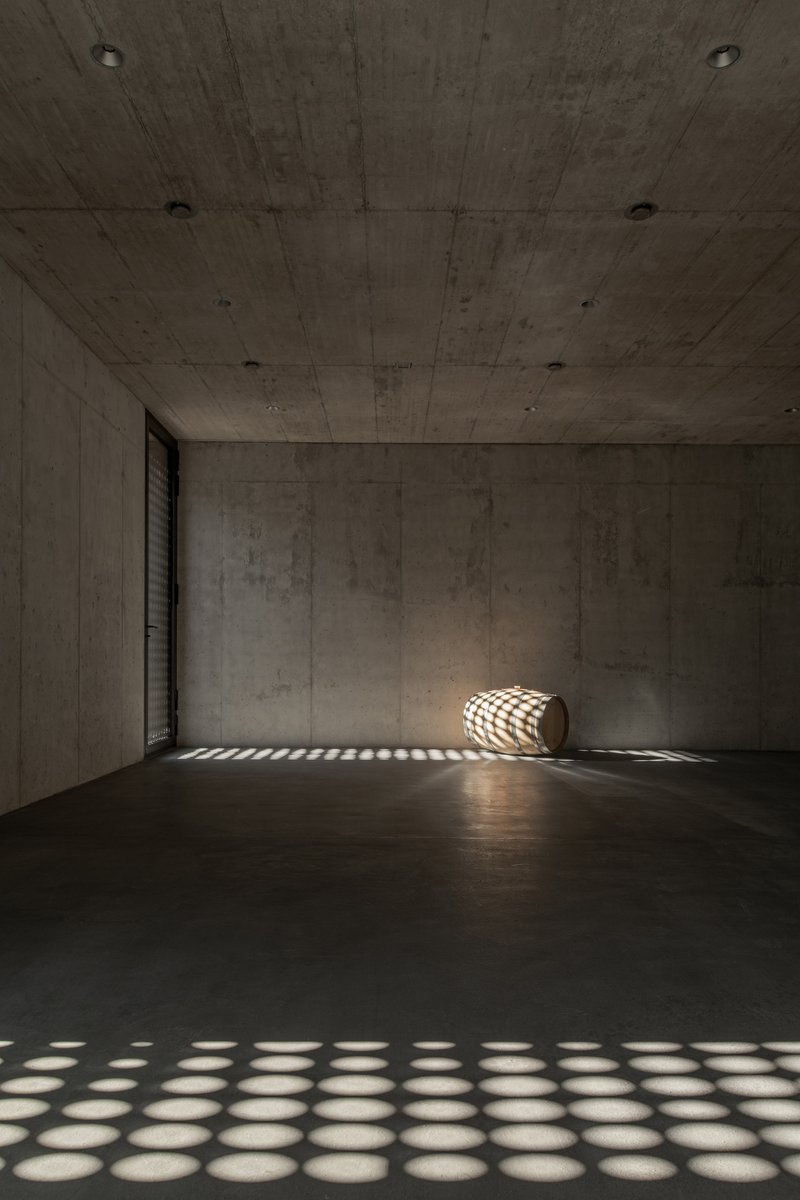 Empty concrete room with a wine barrel casting patterned shadows from a perforated screen