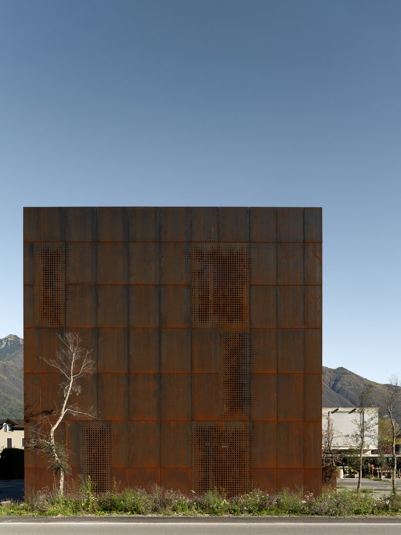 Weathered steel facade with perforated vertical openings beside a bare winter tree