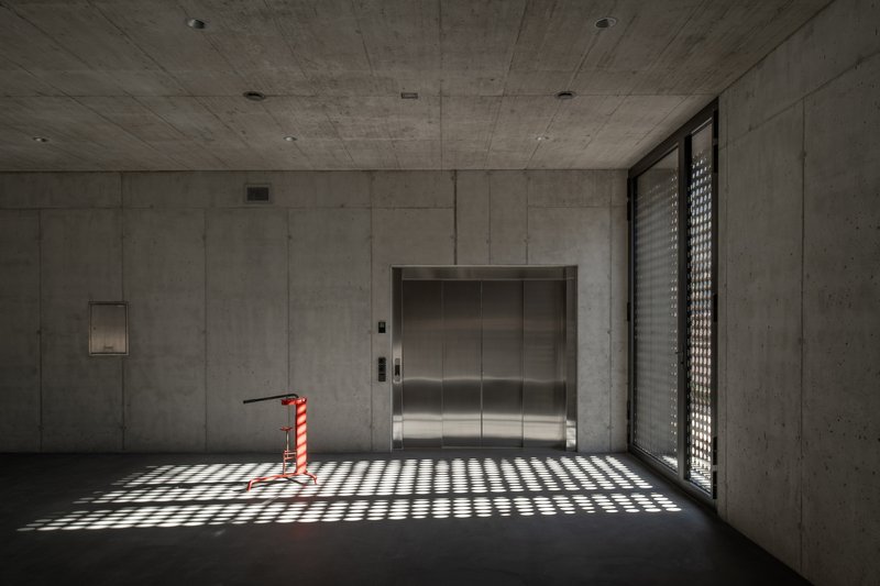 Concrete lobby with stainless steel elevator doors and patterned light from a perforated screen window
