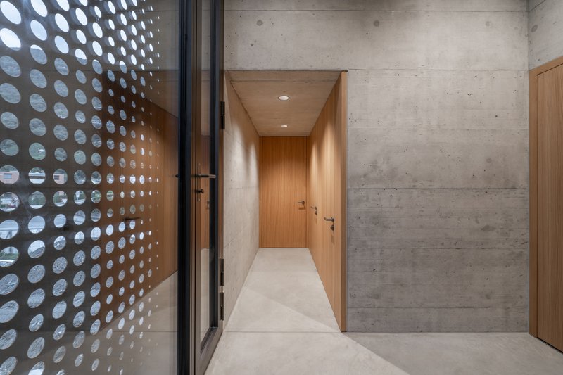 Corridor with timber-clad walls and perforated metal screen casting circular light patterns on terrazzo flooring