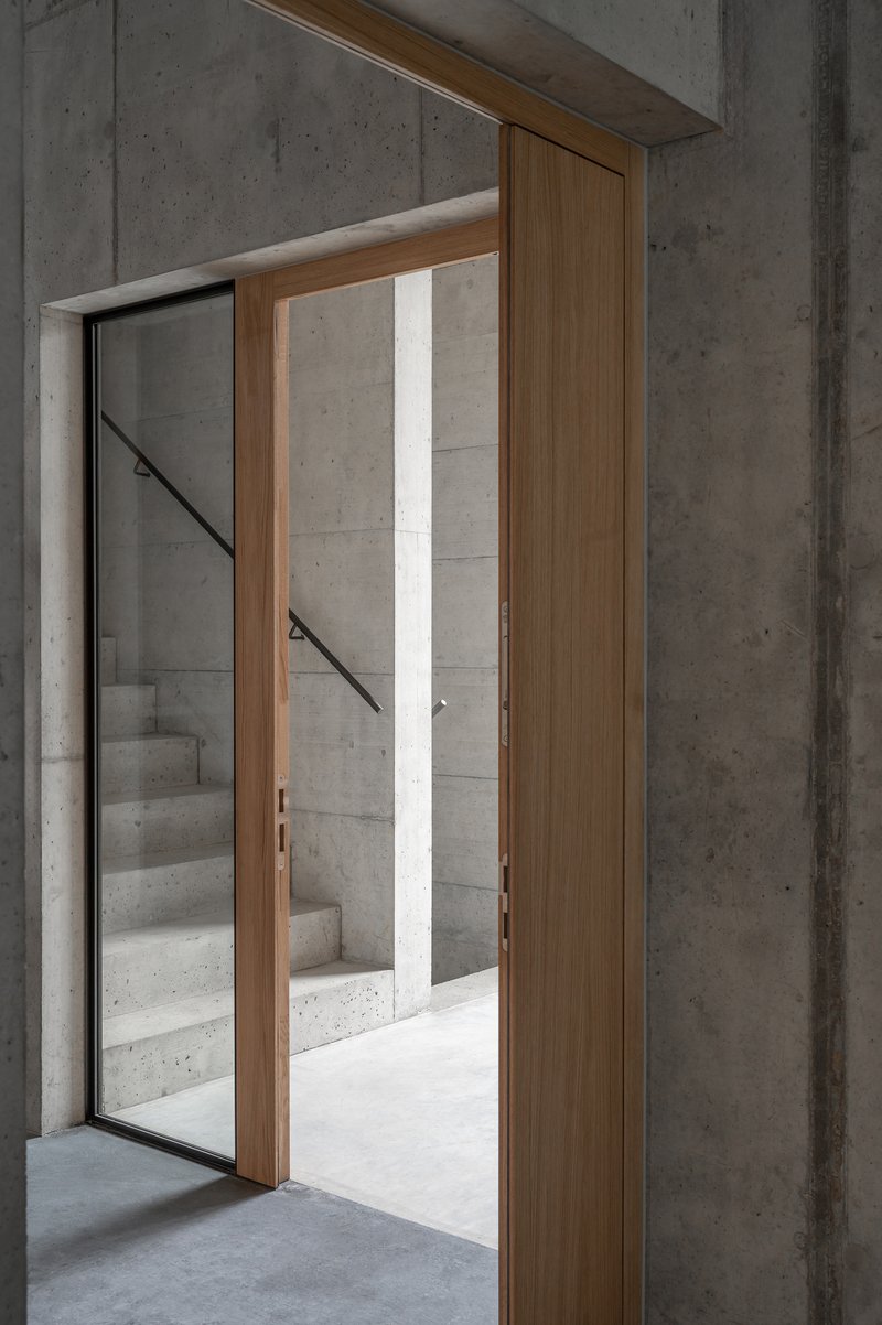 Timber-framed doorway opening to a concrete staircase with metal handrail in daylight