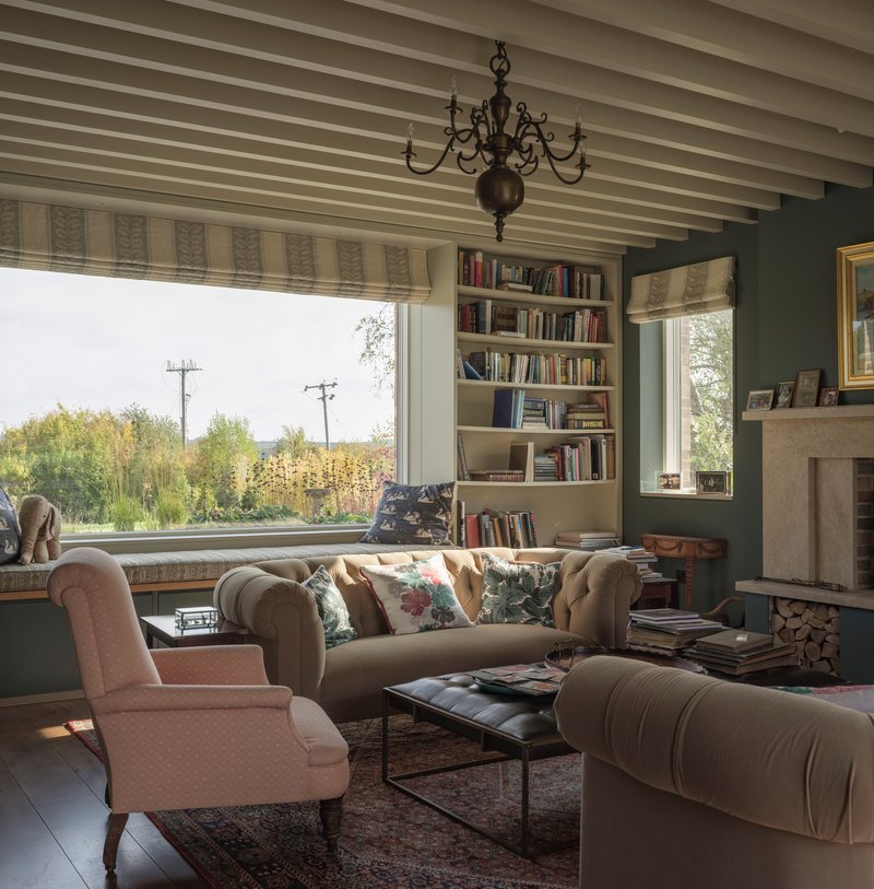 Living room with exposed ceiling beams and large window framing autumn fields beyond built-in bookshelves