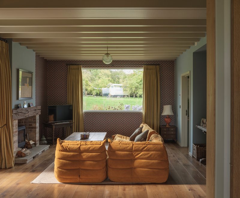 Living room with exposed timber ceiling joists and a landscape window framing green fields beyond