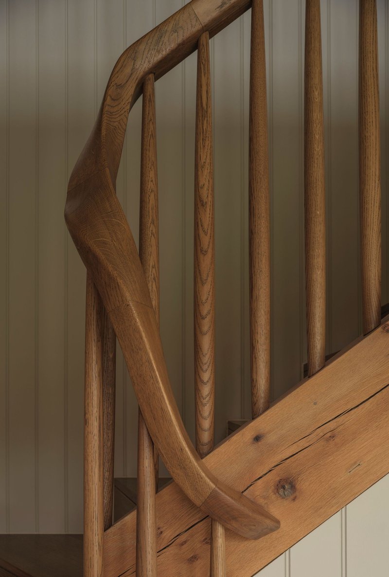 Close-up of curved oak handrail and vertical balusters against painted tongue-and-groove wall panels