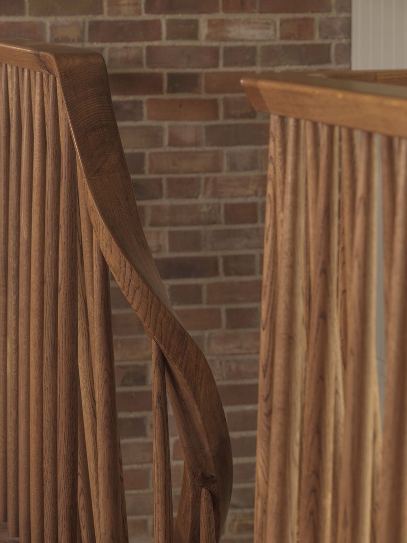 Oak staircase with curved handrail and vertical slats against an exposed brick wall