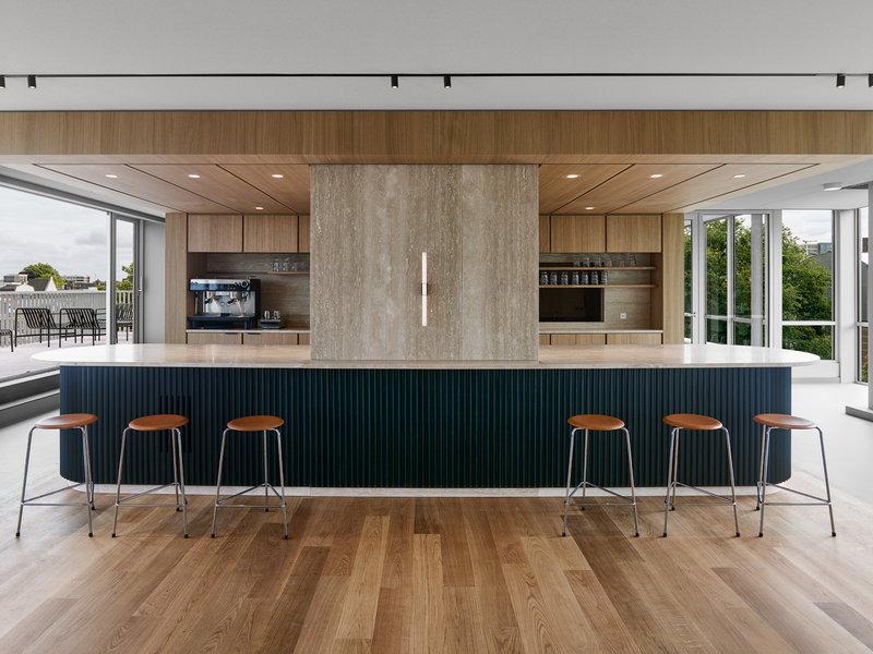 Central island with dark fluted panels and bar seating beneath a timber-paneled ceiling canopy