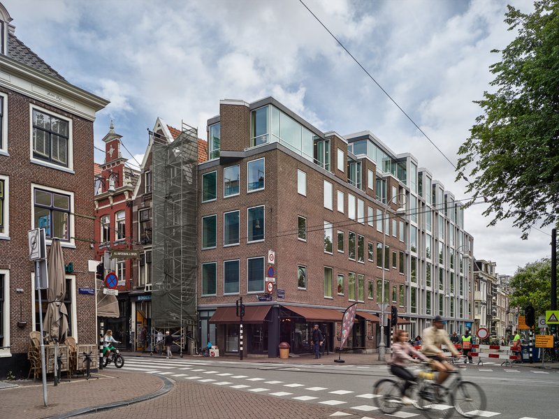 Street view of the mixed brick and glass facade with cyclists passing under cloudy skies