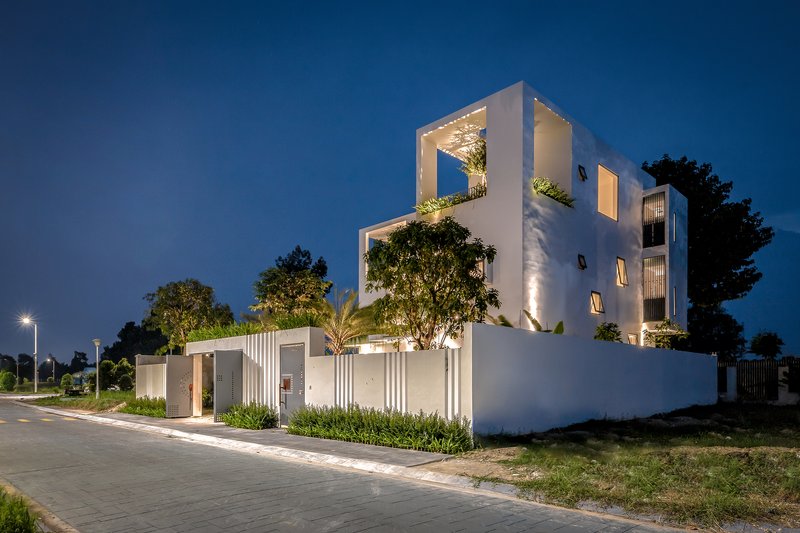 Corner view at twilight showing stacked white volumes with framed tree planters and uplighting
