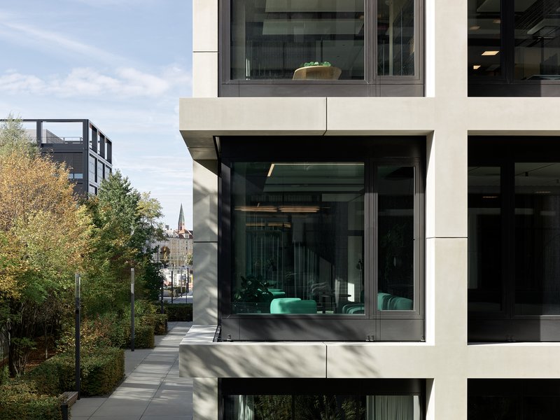Corner detail of cantilevered volumes with floor-to-ceiling glazing revealing green furnishings in afternoon light