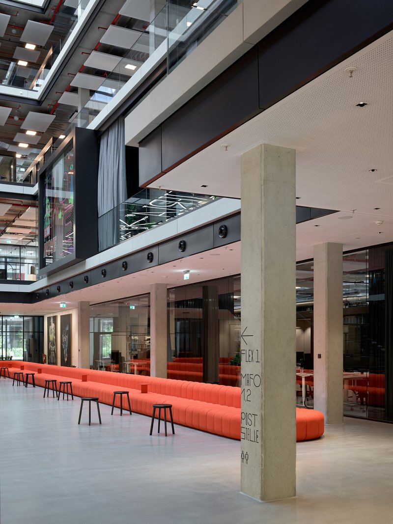 Interior atrium with long orange upholstered bench seating and exposed concrete column in the foreground