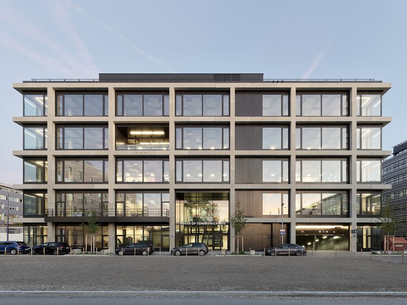 Street-facing facade with precast concrete grid framing floor-to-ceiling windows under an overcast sky