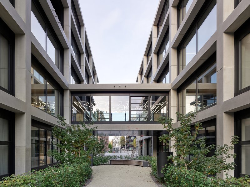 Landscaped courtyard with planted beds and trees beneath two cantilevered glass bridges connecting the wings