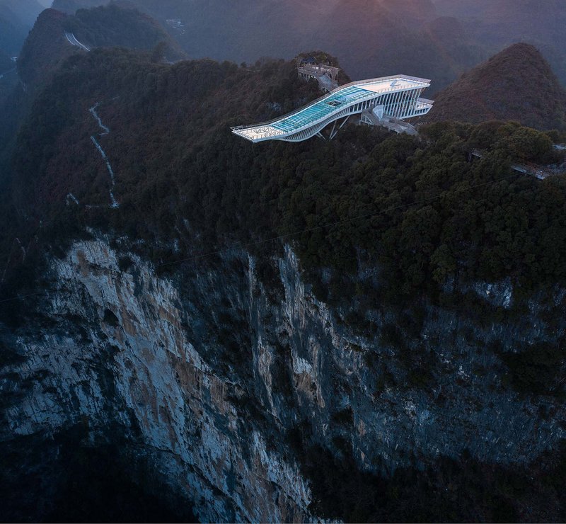 Aerial view of the wing-shaped glass platform perched on a clifftop at dusk with mist
