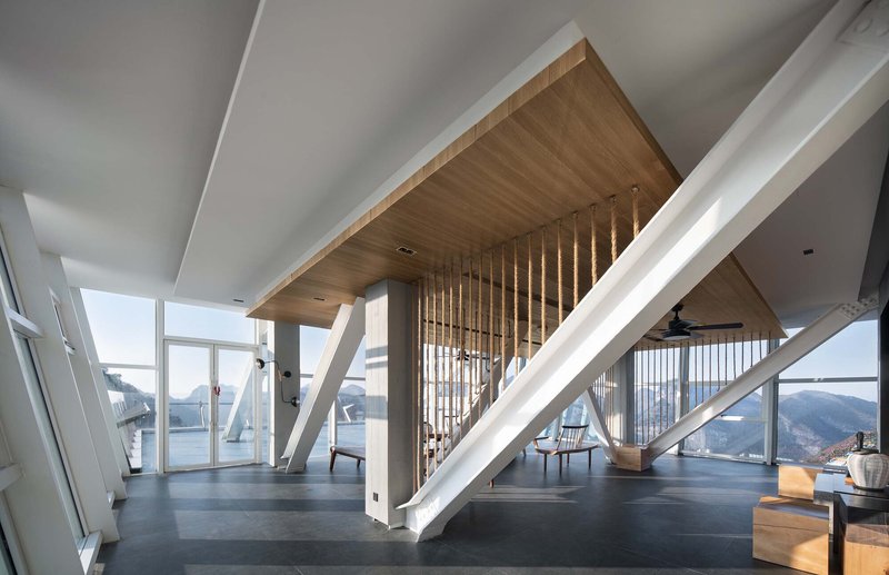 Interior space with diagonal white columns, timber ceiling inset and vertical wood slat screen with mountain views