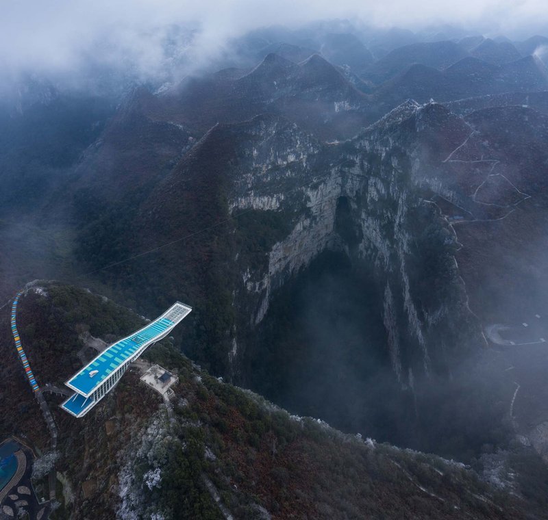 Aerial view of the cantilevered blue-roofed viewing platform extending over a misty mountain gorge