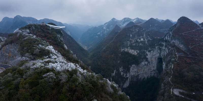 Distant view of the white cantilevered structure perched on a frosted ridgeline above steep valleys