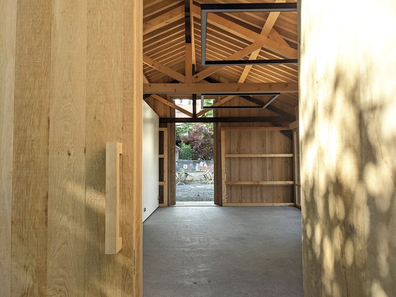 View through timber doorway toward the exposed roof structure with dappled light on plywood walls