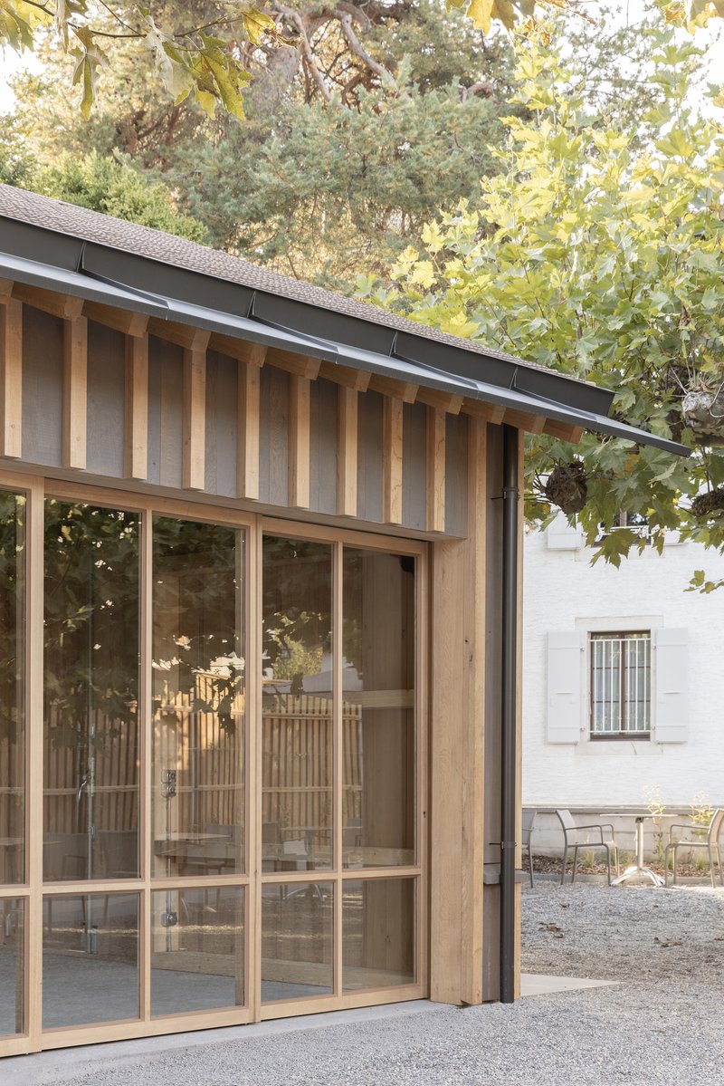 Corner detail of the vertical timber cladding above floor-to-ceiling glazed doors in afternoon light