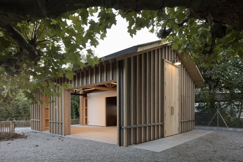 Low pavilion with alternating grey and timber vertical cladding beneath mature trees in autumn