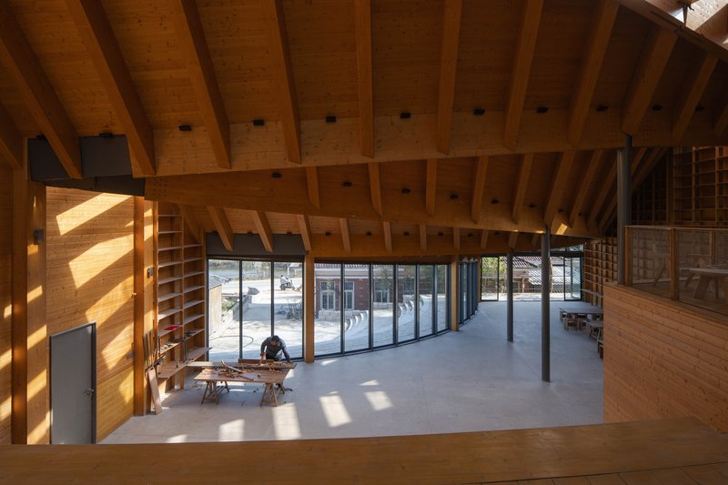 Double-height interior with exposed timber beams and curved glazed wall overlooking a courtyard