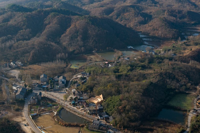 Aerial view of a small village with a timber-clad building nestled among trees and ponds