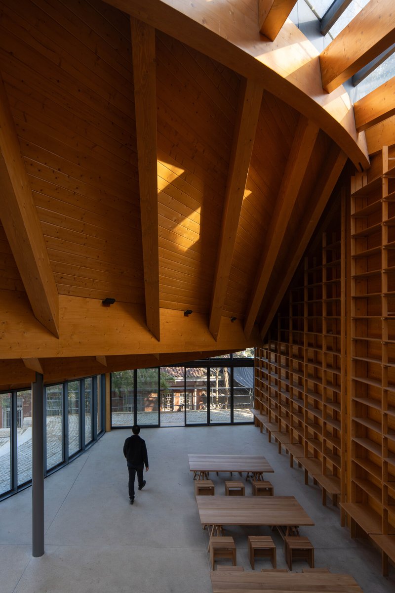 Ground floor entry space with person walking past timber benches below cantilevered beams