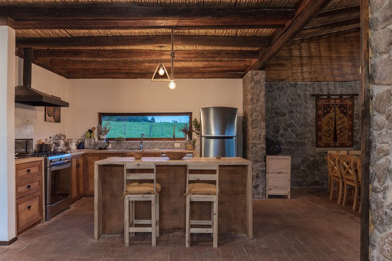 Open kitchen with timber cabinetry, central island and horizontal window framing green pasture beyond